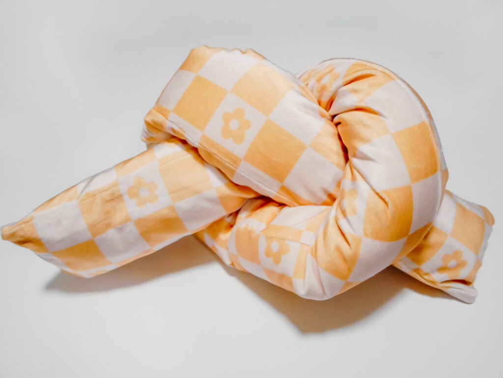 close up of orange and white checkered cushion folded into a knot pillow. 