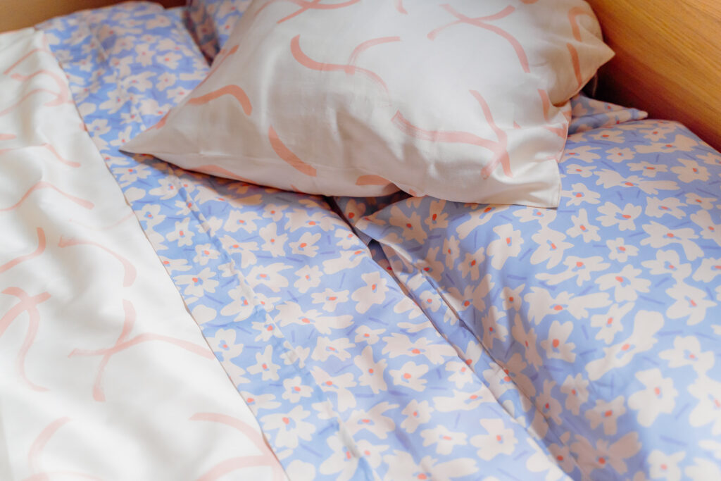 Close up of purple flowered sheets and pillowed cases, and crème pillowed cases matching the crème duvet.