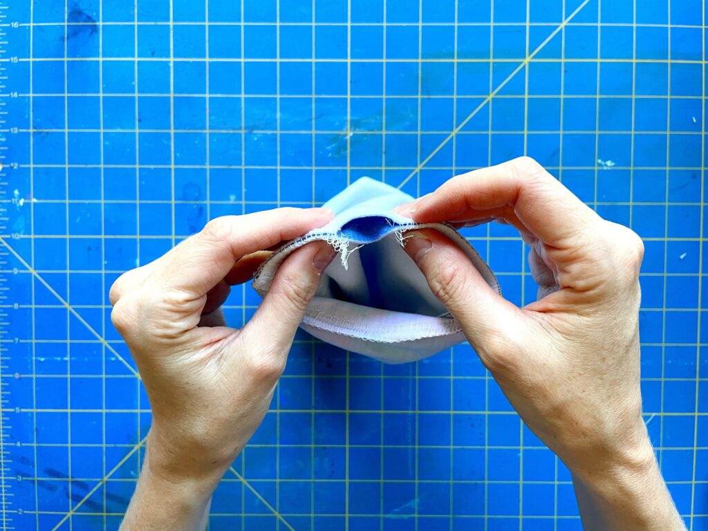 Two hands holding the end of the fabric tube, pinching between an opening. A blue and yellow cutting mat is the background.
