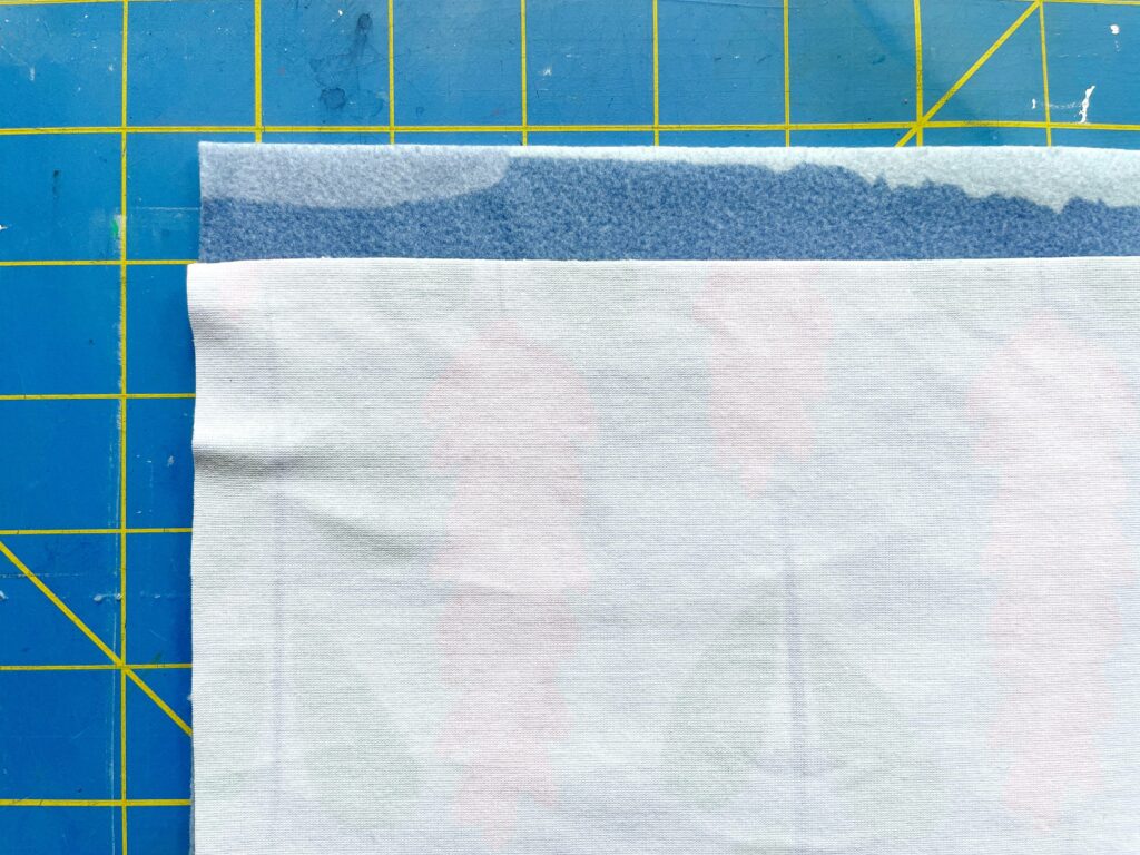 A close-up of two fabric pieces on top of each other. One is turned right side in and slightly below the first fabric. A blue and yellow cutting mat is the background.