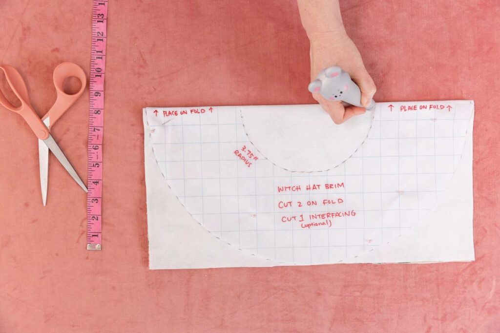 Keiko traces out the lines for the inner circle on the folded-in fabric using the grid-papered template. Peach colored scissors rest beside a measuring tape.