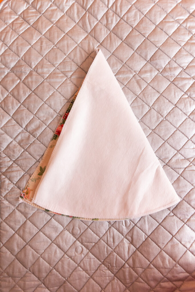 A sewn together piece of fabric and heavy interfacing are folded in half, in a cone shape. A silver ironing mat is in the background.