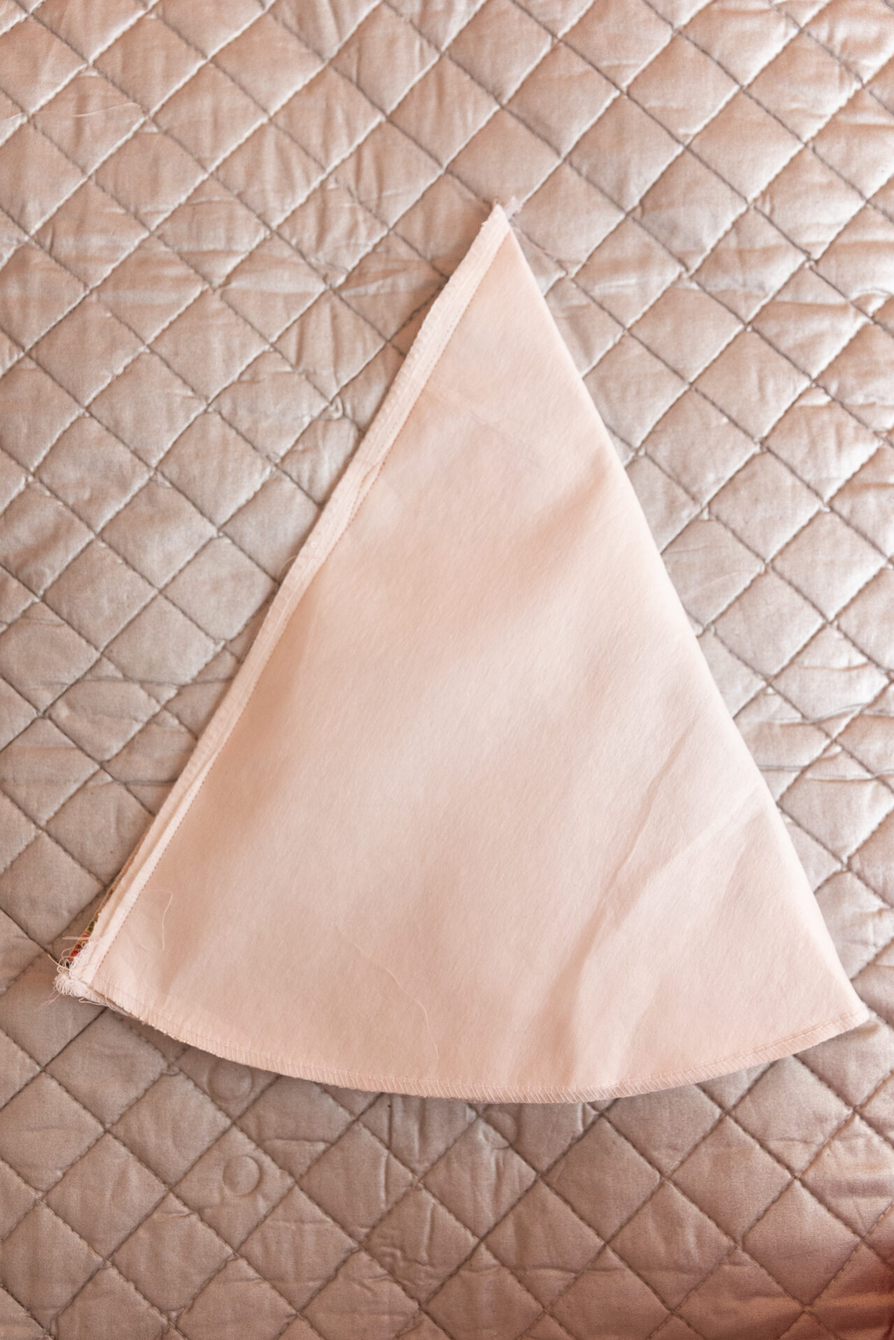 A white cone lays on a silver ironing mat. The left side is sewn down horizontally before preparing to attach it to the brim.