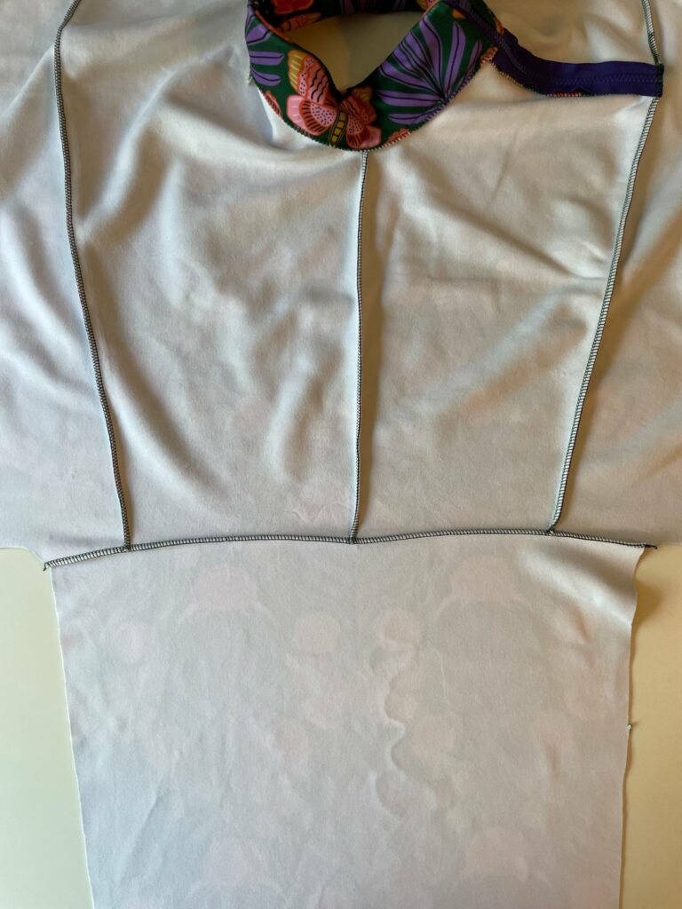 The jacket is turned wrong side up to show the arm fabric is sewn to the shoulder.  A white surface is in the background.