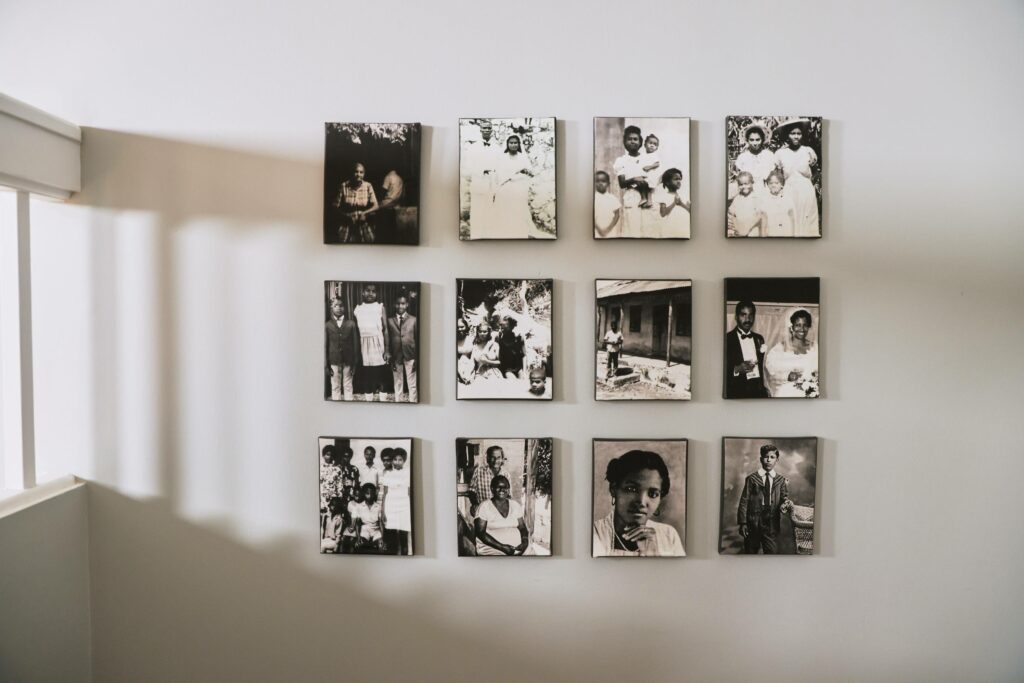 Twelve antique family photos are on twelve square canvas on a light grey wall. The shadow from the staircase beam can be seen through the photos. 