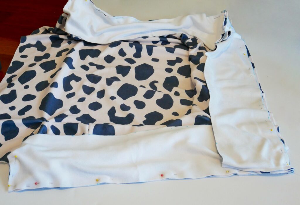 The entire bolster is pinned right side out to the base of the dog bed, which is right side up. The fabric is white with black cow-print shapes.