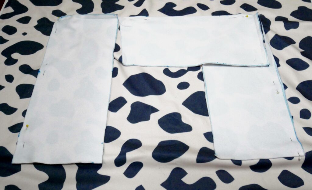 Two longer side inner bolster pieces lay wrong side up and parallel to each other. A shorter center piece is placed at the top of the two parallel side pieces, forming a U. These fabric pieces are on top of fabric that is white with black cow-print shapes.