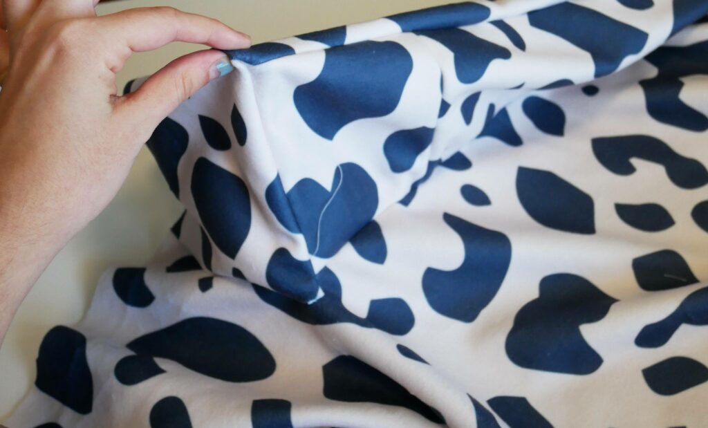 Attaching the rectangle sides of the Inner Bolster together where they meet the Bolster Base. The end of one side of the Inner Bolster has been closed with a small square piece of fabric. The fabric is white with black cow-print shapes.
