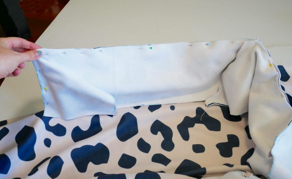 A hold holds up a corner of the inner bolster piece with the wrong side facing out. It is laying on on top of fabric that is white with black cow-print shapes.