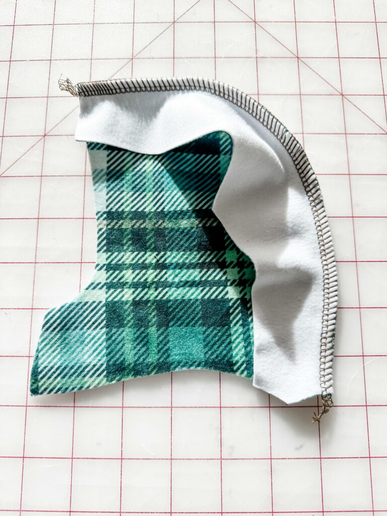 A green-and-white plaid hood is in the process of being sewn. Half of the hoodie is shown design side up and has been sewn to the center piece of the hoodie, which is design side down.
