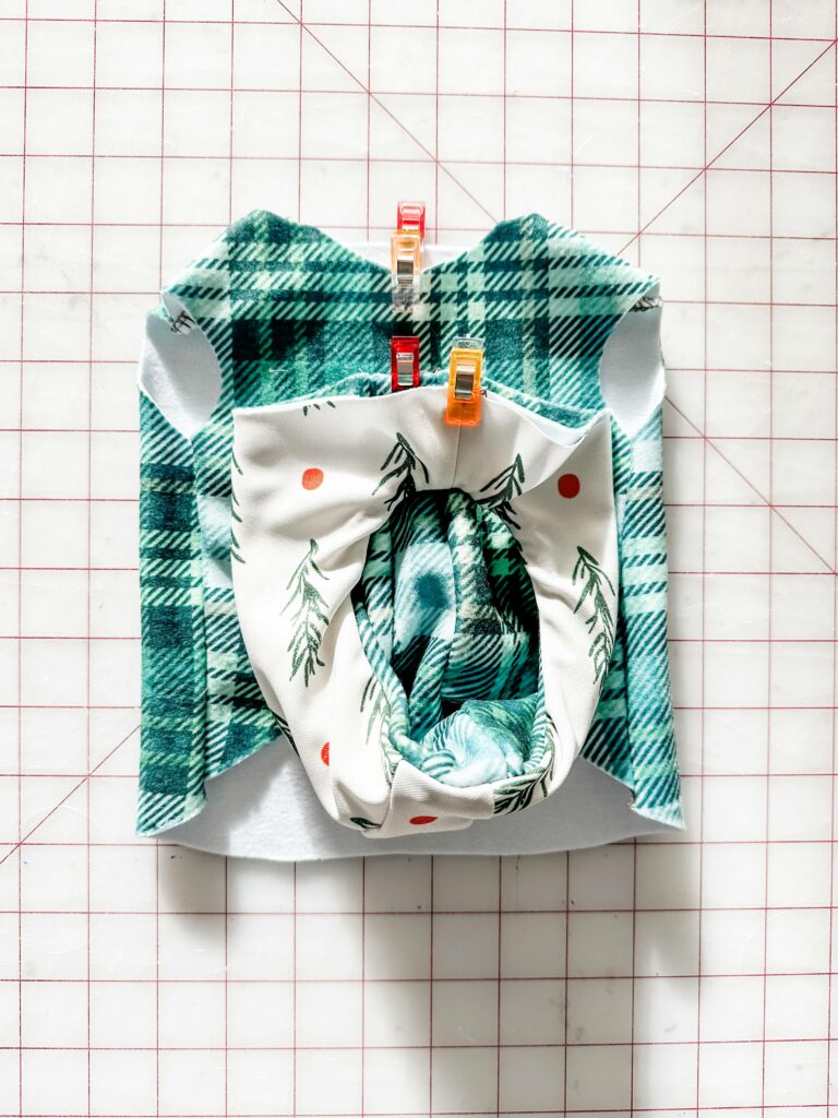 A green-and-white plaid hood is flipped inside out and rests on top of a green-and-white plaid bodice. The fabric lays on a white cutting mat with a red grid.