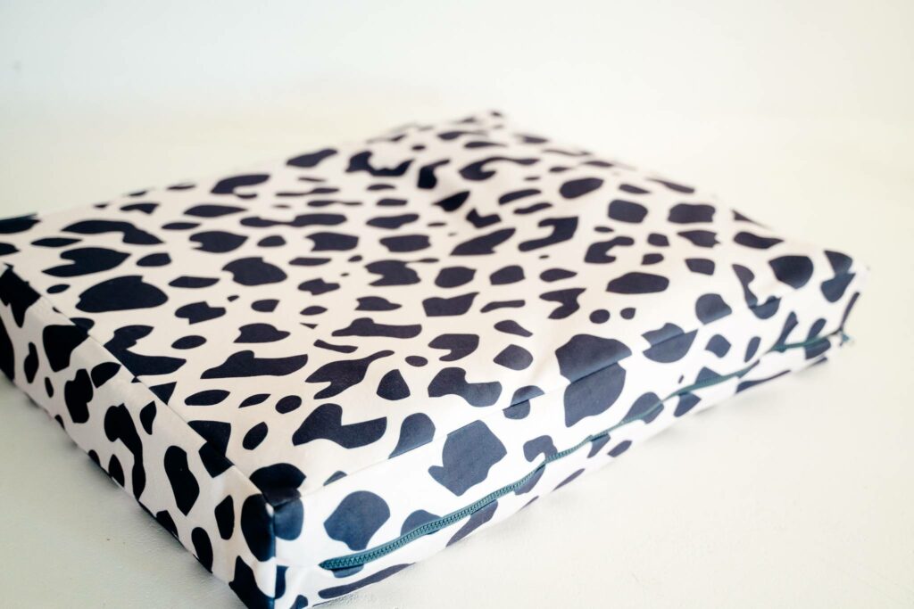 Image of the finished rectangular dog bed made in fabric that is white with black cow-print shapes. It has a black zipper enclosure.