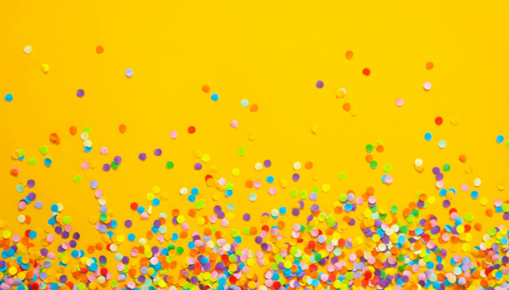 A top-down view of a bright yellow surface scattered with round rainbow confetti.