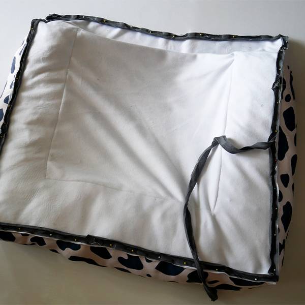 The rectangular dog bed has been flipped over so that its all-white bottom is shown. Black bias tape is being pinned around all four edges of the bed.