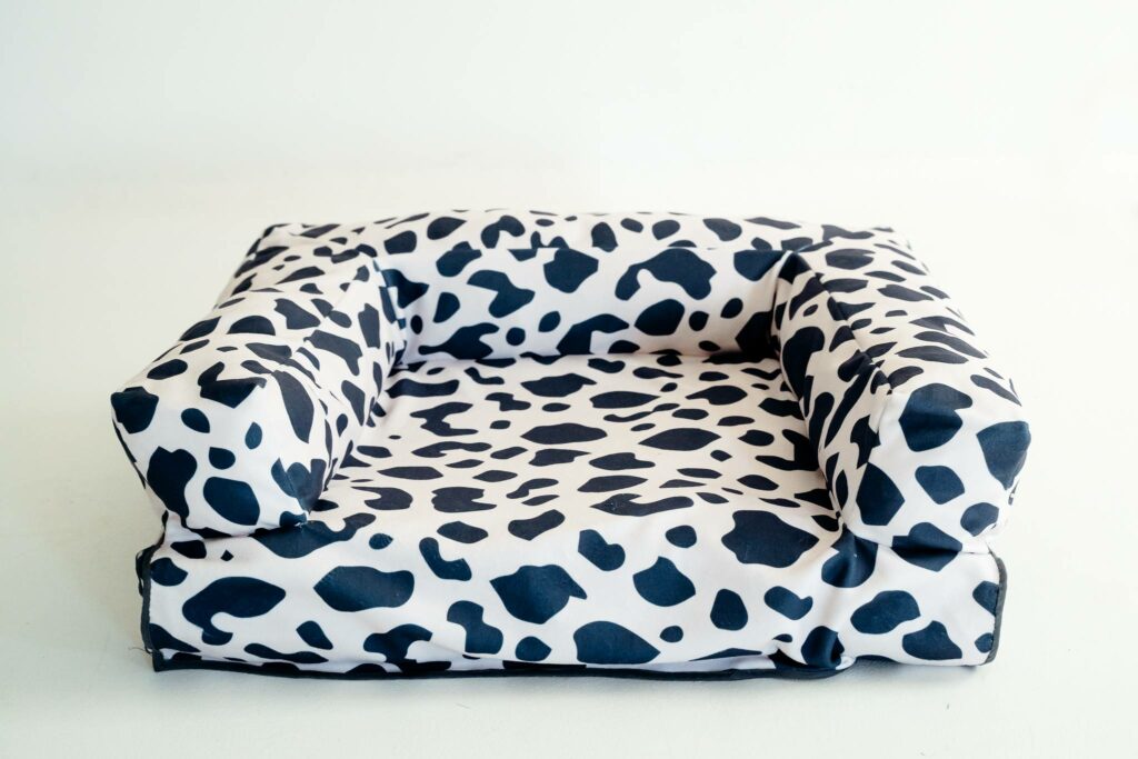 Image of the finished rectangular dog bed made in fabric that is white with black cow-print shapes. The bed has a rectangular base and a U-shaped bolster at the back and two sides.