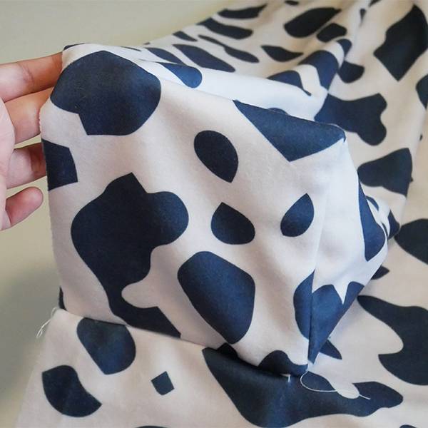 After sewing the small square sides connecting the top bolster together where they meet the Bolster Base. The fabric is white with black cow-print shapes.
