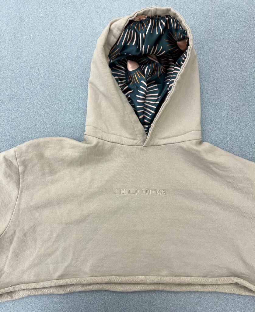 A tan hoodie lays on a grey table with a satin inside.