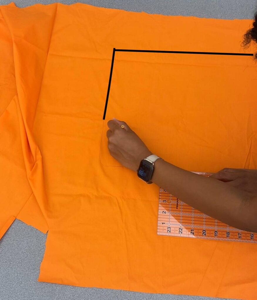 Arlette tracing the curve of her hood on the orange template fabric. Her sewing ruler rests on the edge of the fabric.