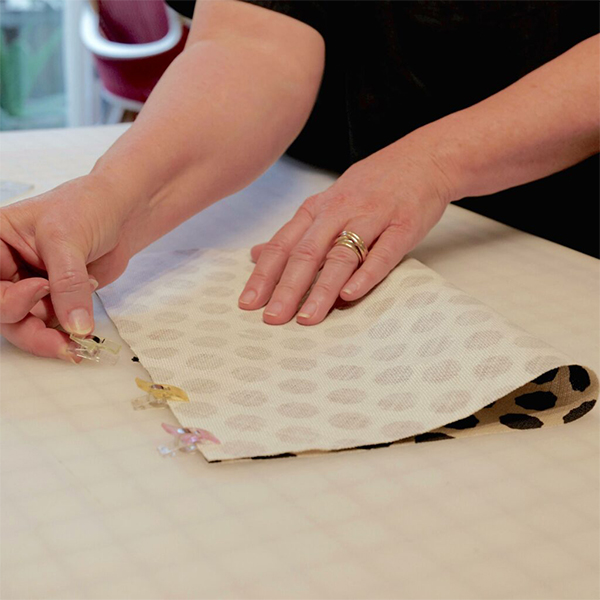 Cinne folds the one of the bag’s main body pieces in half vertically and clips the top and bottom together. The edges are unclipped in preparation for sewing them together.