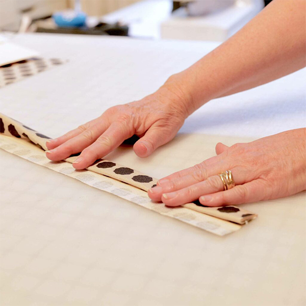 Folding the center of a long thin strip of fabric with a folding guide made from a strip of paper cut from a manila folder.