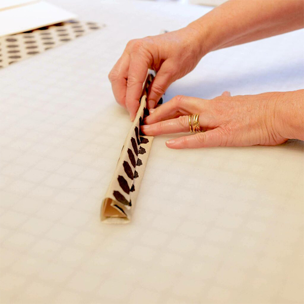 Folding the final side of a long thin strip of fabric with a folding guide made from a strip of paper cut from a manila folder.