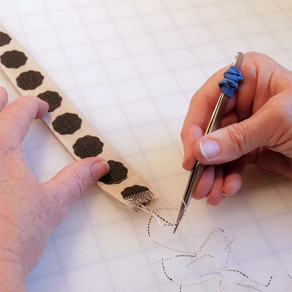 Using tweezers to fray the ends of the long thin fabric belt by hand.