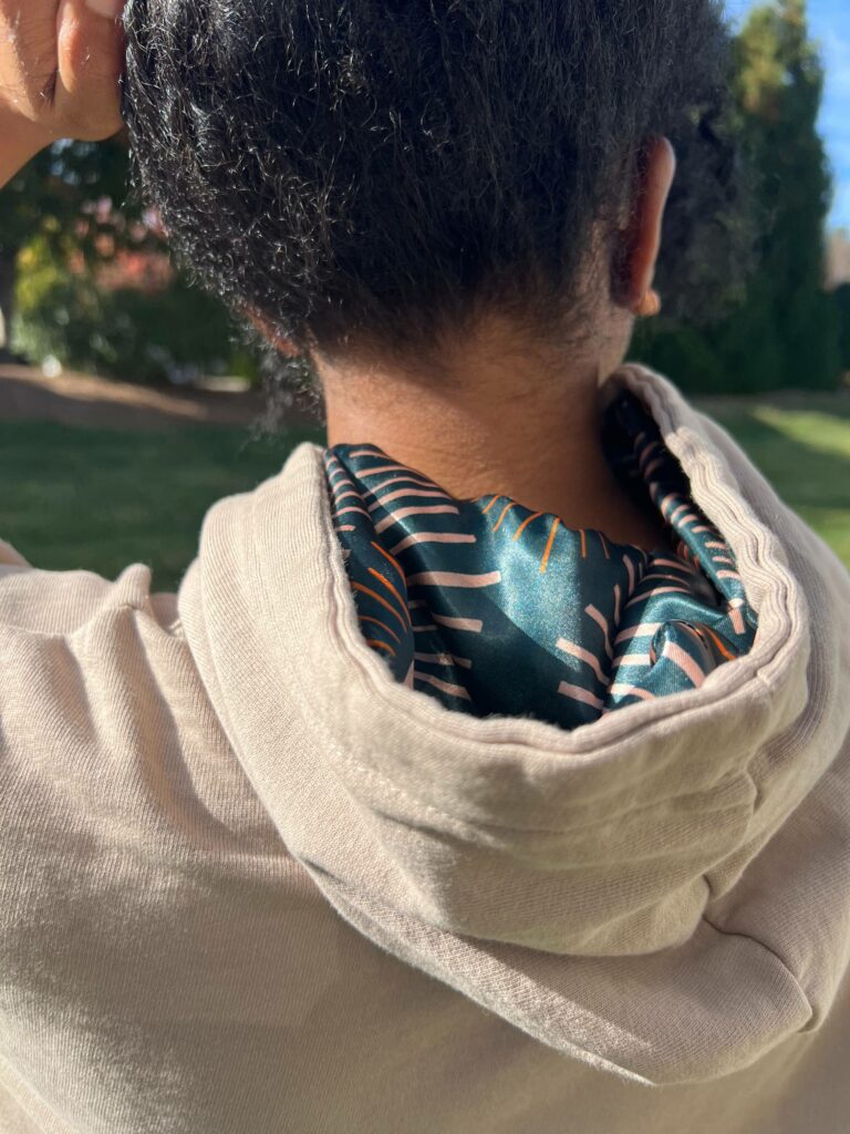 A close-up of Arlette’s satin-lined hoodie. From the back of her head, we see the inside of her hoodie which is lined with a forest green satin design.