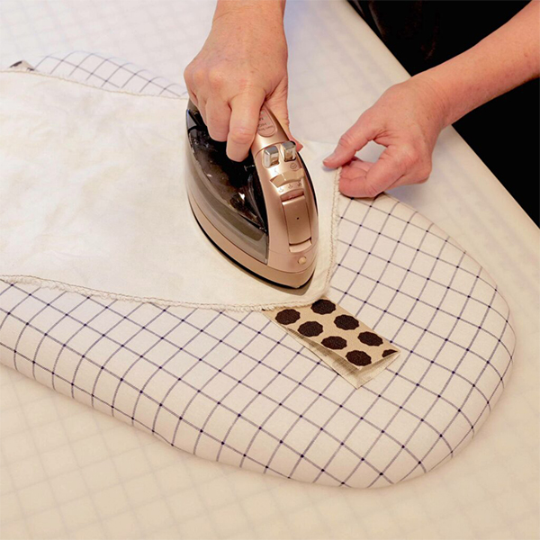 Cinne is ironing a long piece of fabric, which has been folded in half lengthwise. The fabric has black dots with a white background. The ironing board cover is white with a black tie grid.