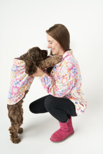A girl and her brown dog are in matching pullover jackets in front of a white background.