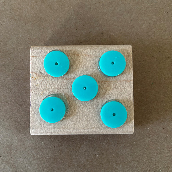 Blue beads are glued to a stamp mount are on a brown surface.