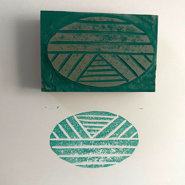 The block print covered in green rests above the print of the design on a white sheet of paper.