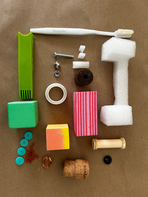 Random objects like foam, beads, sponges, wine cork, a toothbrush, and hardware lay on a brown surface.