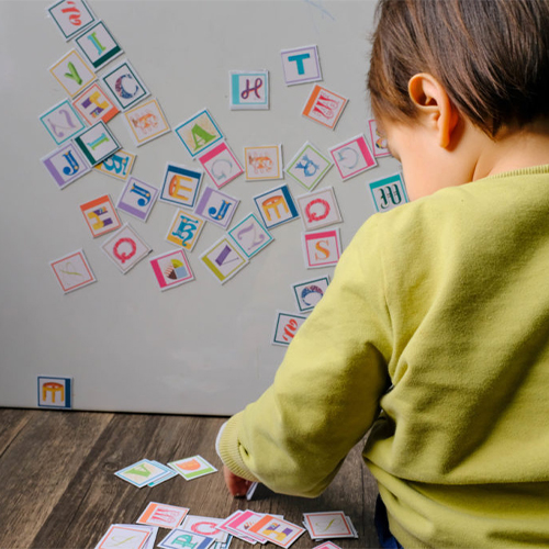A child plays with magnetic alphabet letters stuck to a white metal surface and made and cut out of Peel and Stick wallpaper.