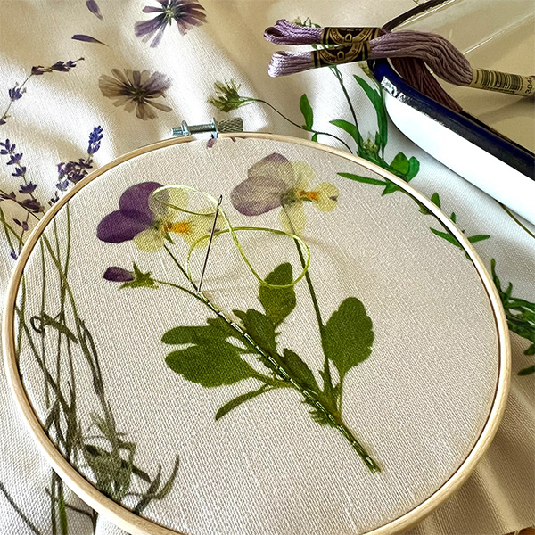 A tea towel is secured in an embroidery hoop with a needle sticking out of the towel.
