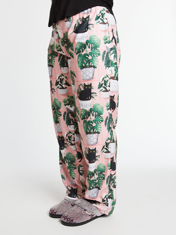 A close up of pink loungepants with a repeating design featuring black cats and green plants in a white planter.