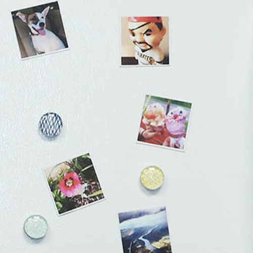 Several small square photo magnets are stuck to a white fridge. The magnets each include a photo of the following: a dog, a bobblehead, ice cream cones, a flower and a photo of a river from far above.