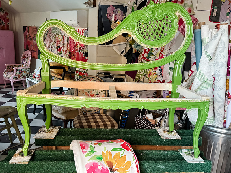 A green painted settee chair on a saddleback with folded floral fabric under it.