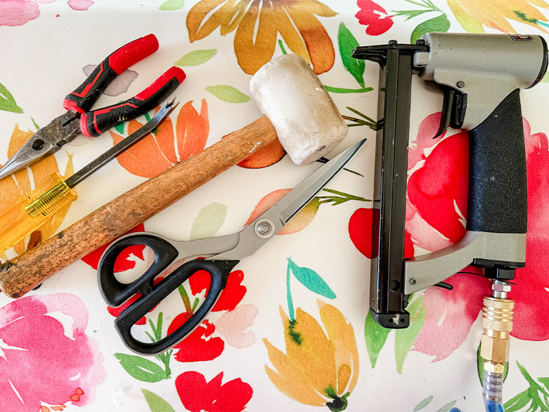 Pliers, a staple lifter, mallet, scissors and electri stapler rest on a floral background