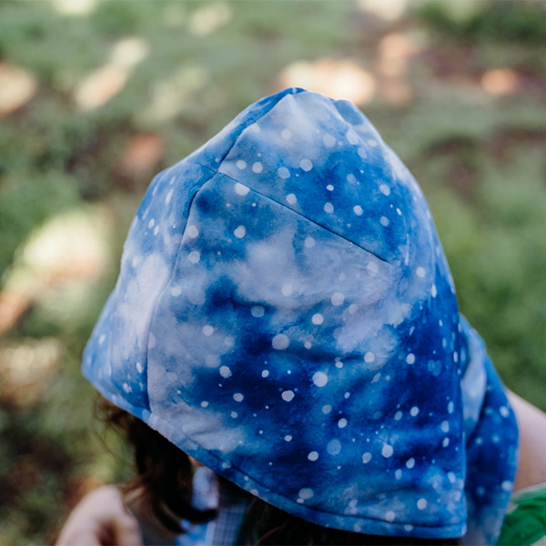 The top view of the hooded scarf where four parts of the scarf meet in the middle of the wearer's head. The fabric is blue with small white circles in different sizes, like snowflakes.