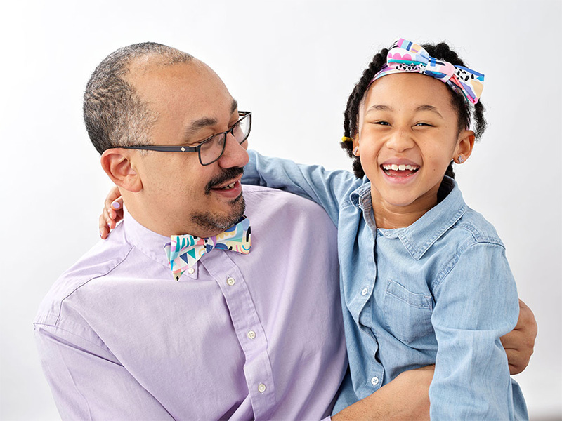 A man wearing a bowtie is looking at a smiling little girl wearing a matching headband.