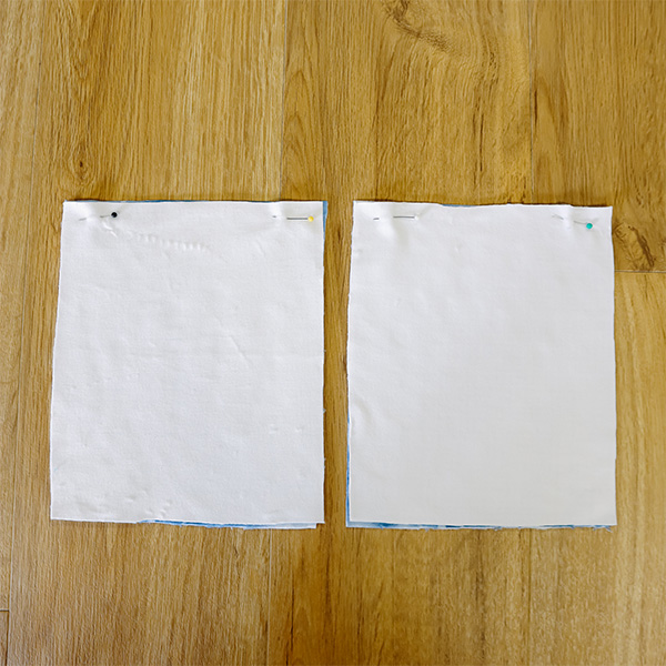 Two fabric squares pinned together with the design sides facing. The squares rest on a wooden background.
