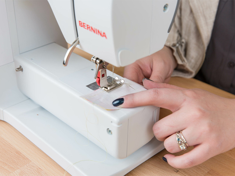 A woman is stitching the rectangle piece of fabric that was pinned.