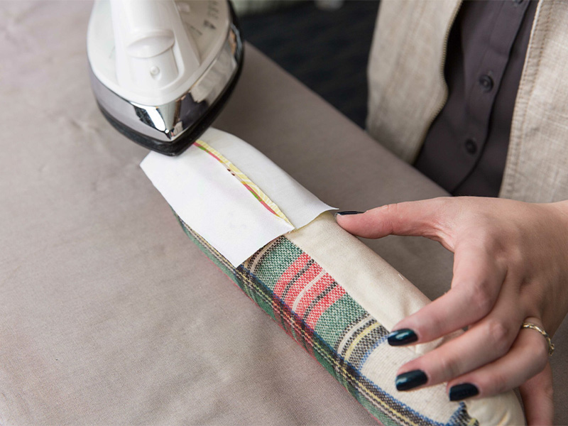 A woman is ironing the seams open of a rectangle piece of fabric using an iron and tailor's ham.
