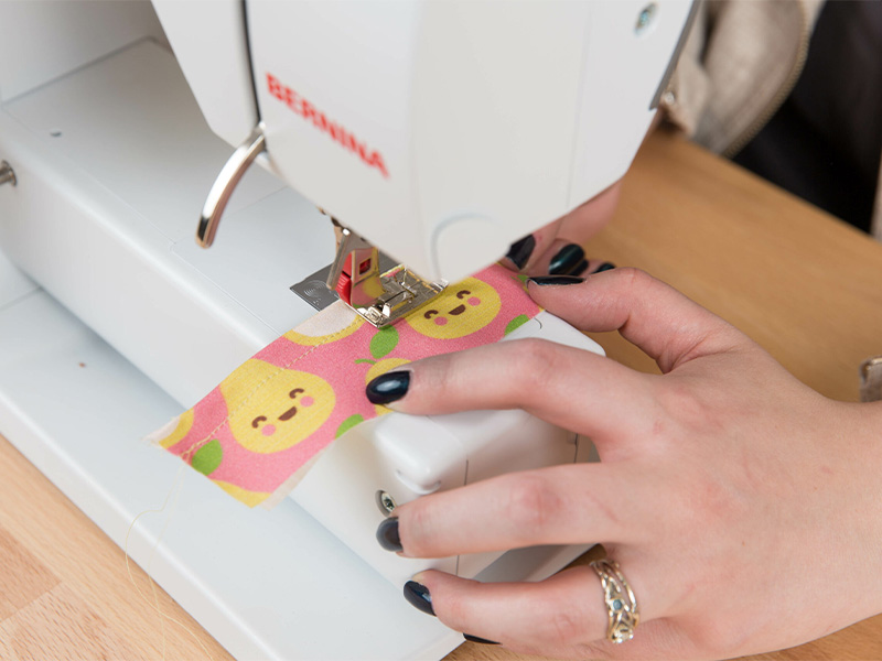 A woman is stitching an elastic casing on a piece of fabric using her sewing machine.
