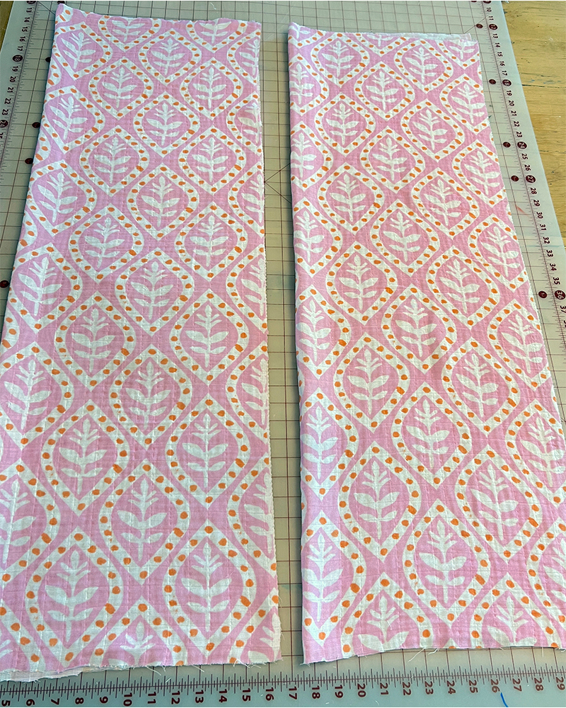 Pressing fabric for the caftan with an iron. The fabric design is repeating white flowers on a pink background. Each flower is encircled by a white oval with orange dots.