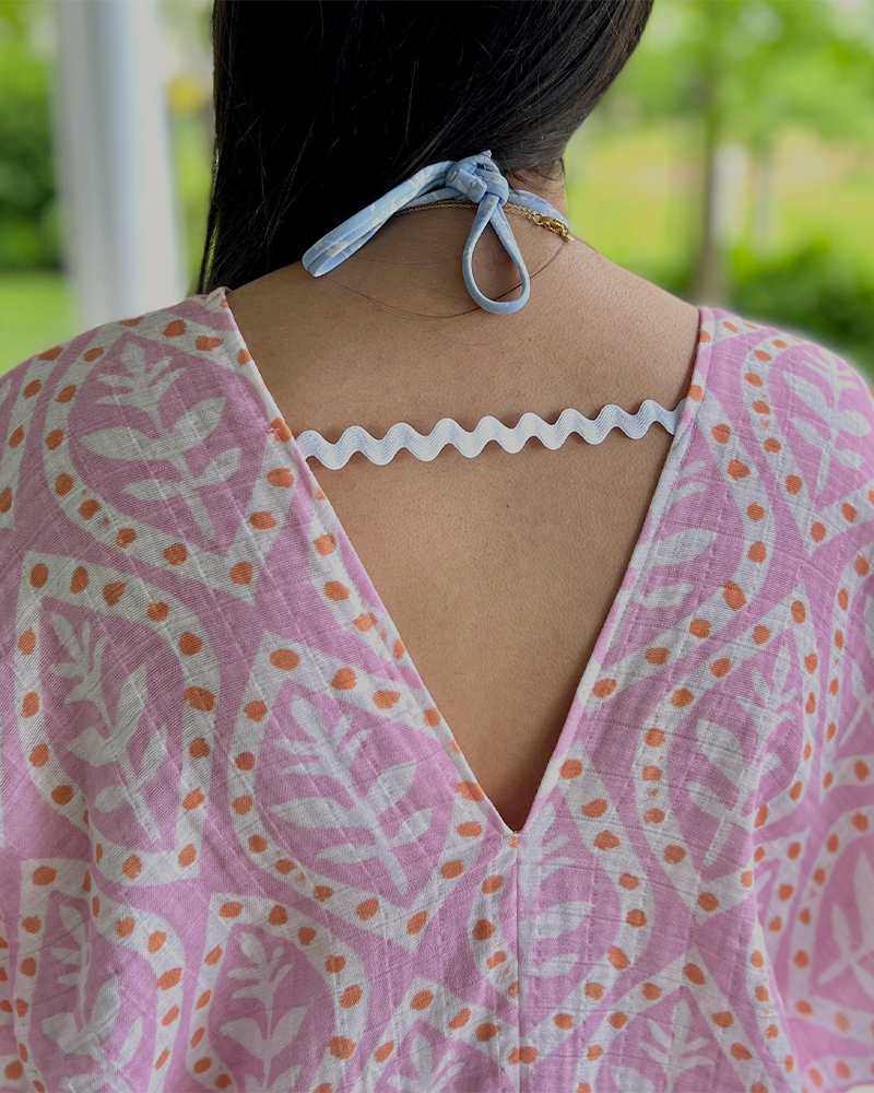 A look at the back of the caftan with a white rick rack closure. The fabric design is repeating white flowers on a pink background. Each flower is encircled by a white oval with orange dots.