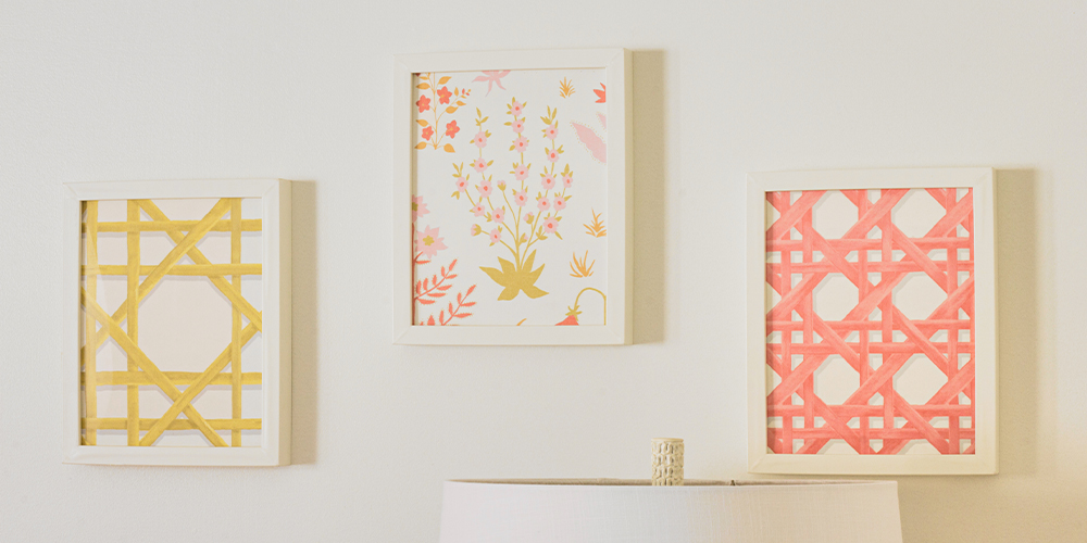 A close up of three of the framed wallpaper swatches, each swatch has been placed in a white frame. From left to right, the wallpaper designs are: a yellow trellis on a white background, small pink flowers with green leaves on a white background and a pink trellis on a white background.